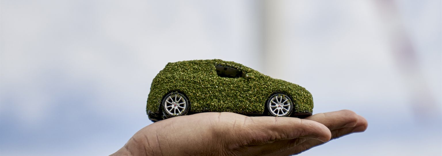 Coche sostenible sobre una mano con aerogeneradores al fondo