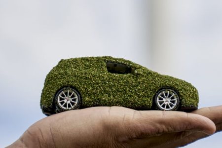 Coche sostenible sobre una mano con aerogeneradores al fondo