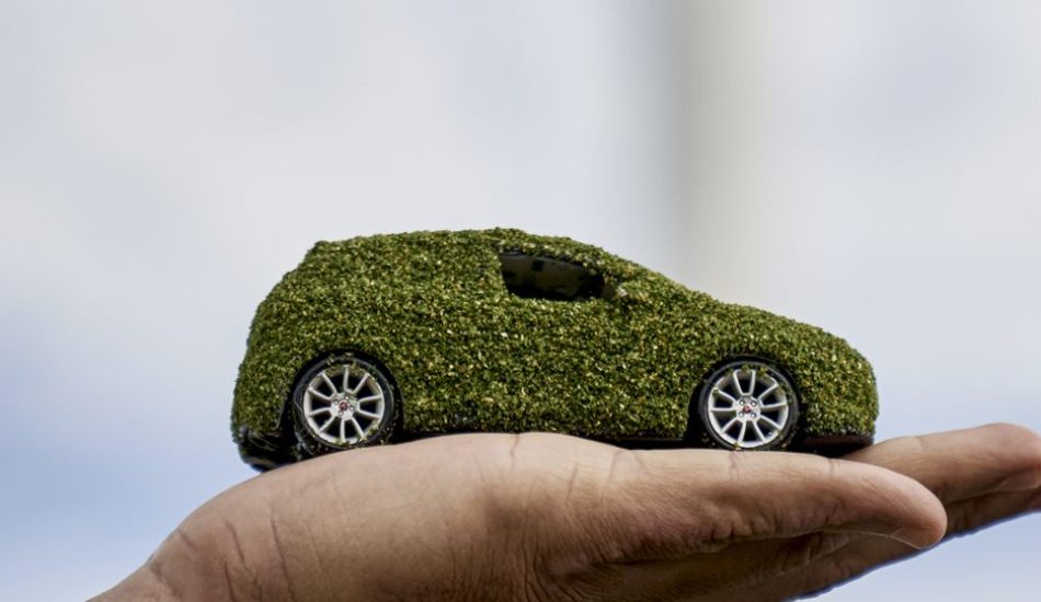 Coche sostenible sobre una mano con aerogeneradores al fondo